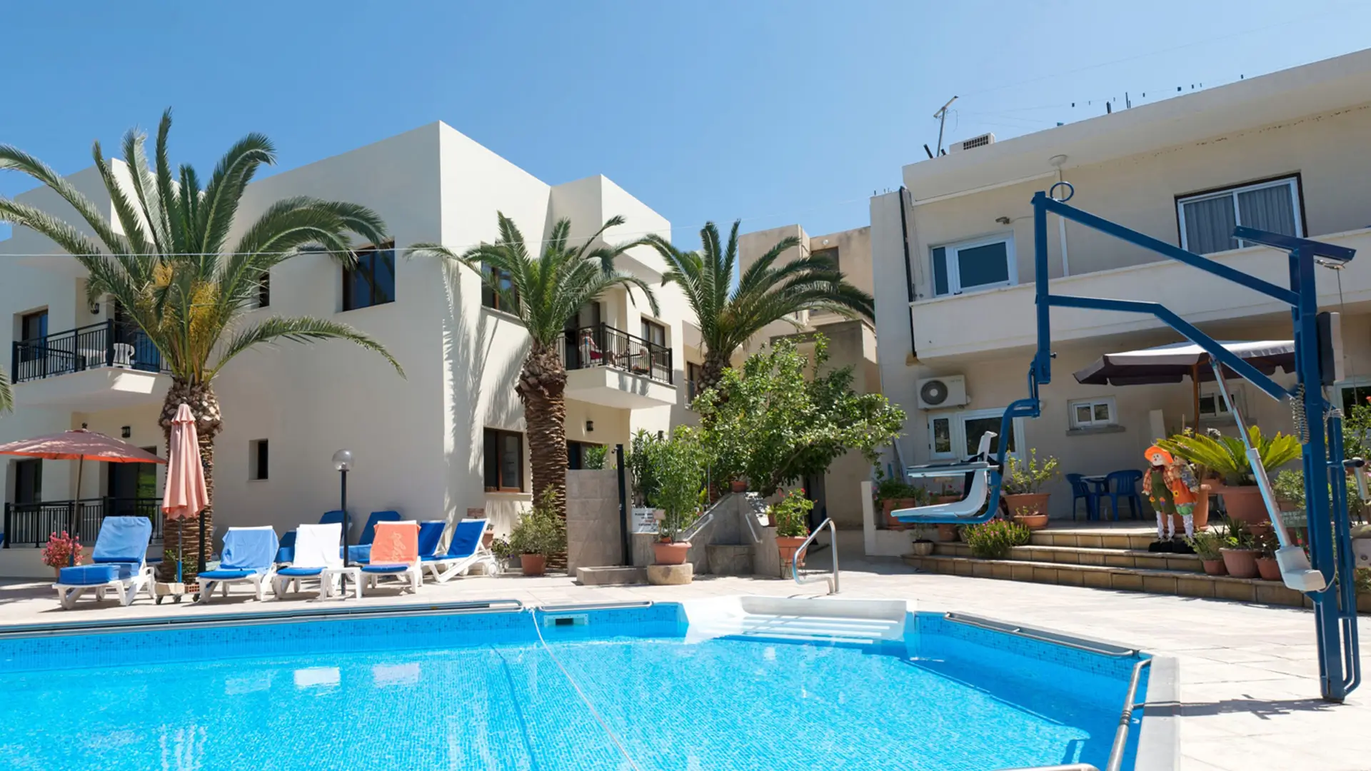 Pool with hoist lift beside white villa buildings.
