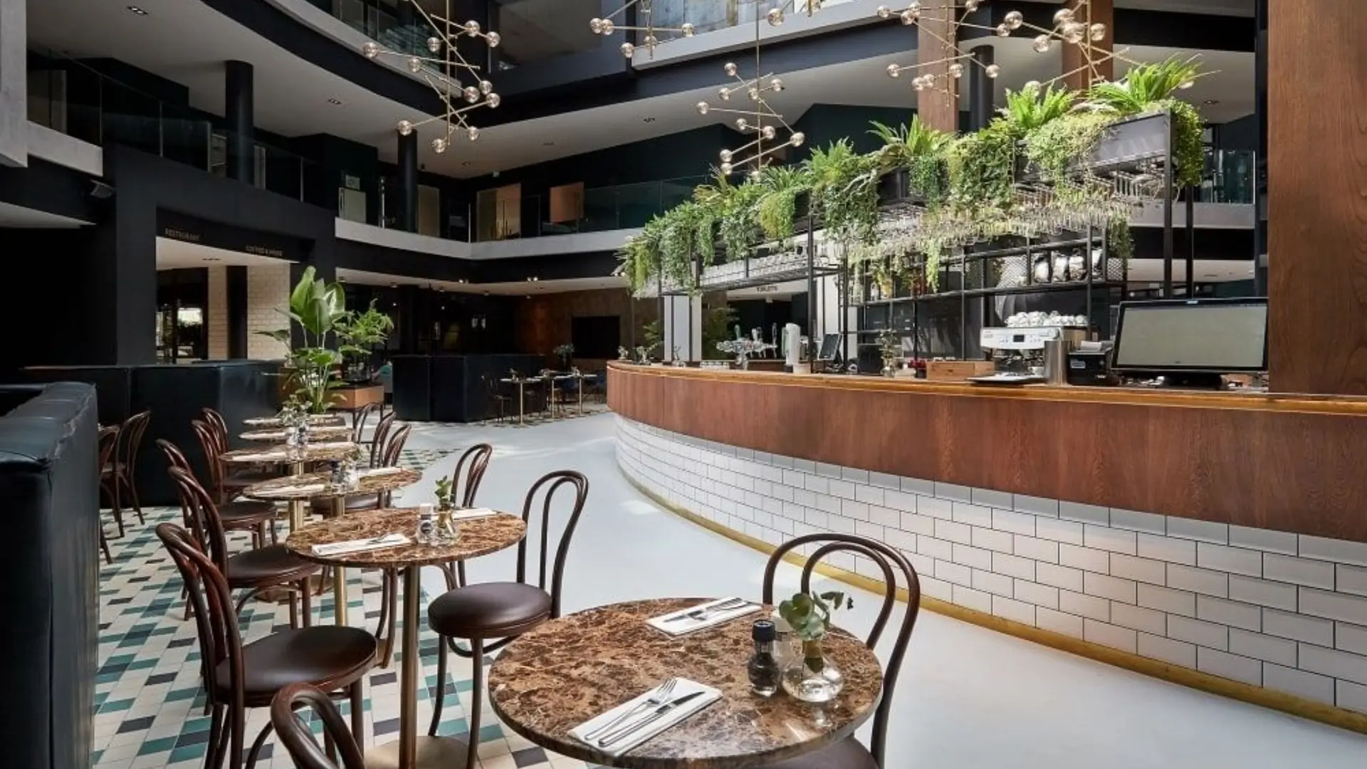 Hotel atrium bar with hanging plants and cafe tables.