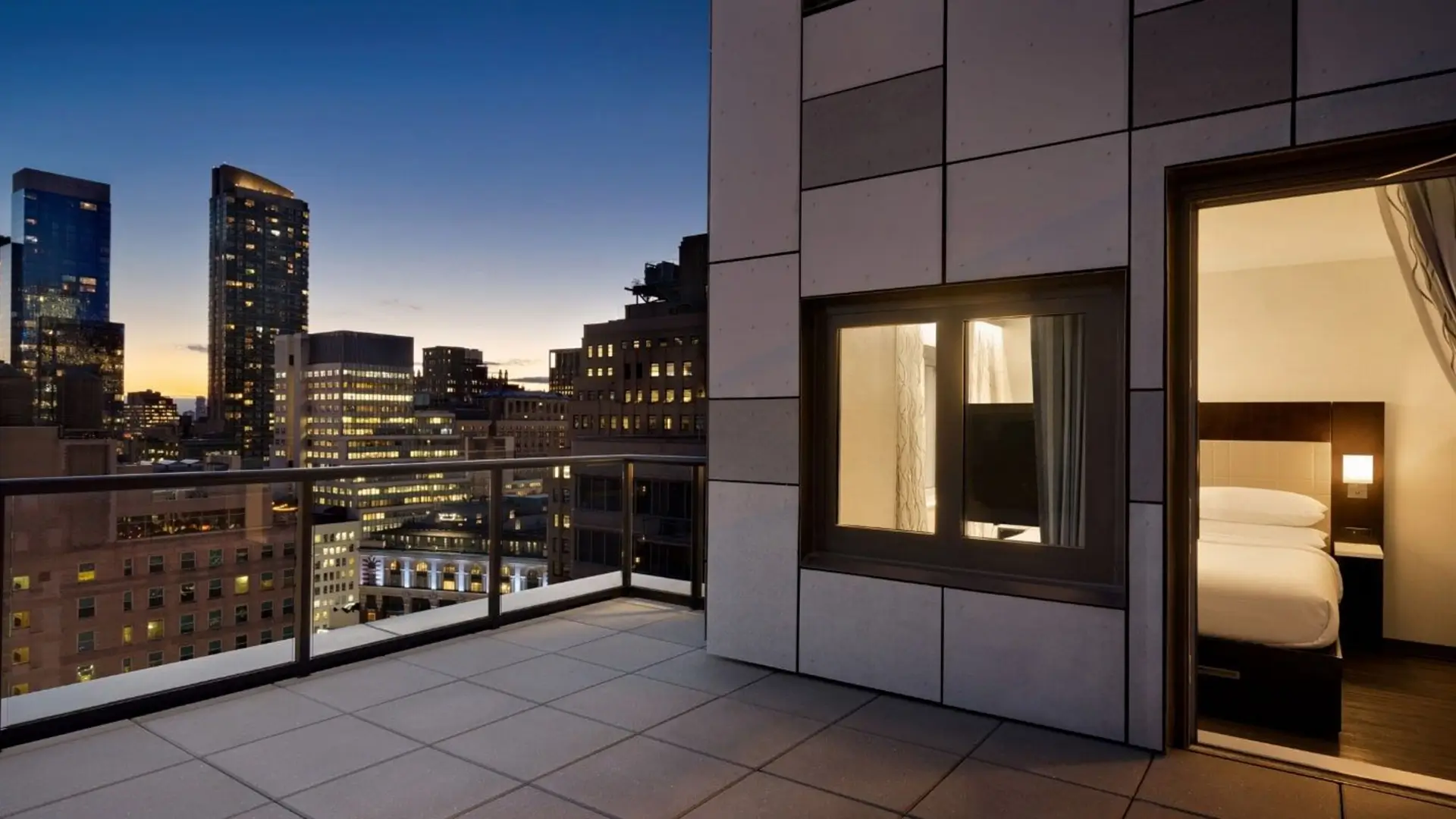 Hotel balcony overlooking city skyline at dusk.