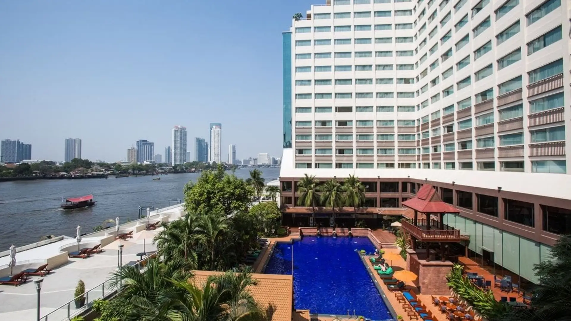Riverside hotel pool with city skyline view.