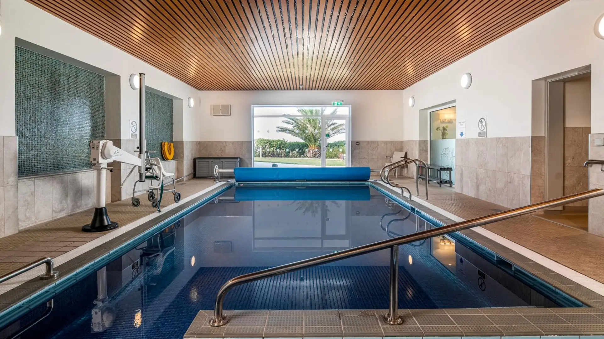 Indoor accessible pool with mobility hoist and garden view.