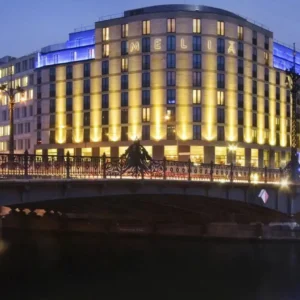 Illuminated Meliá hotel at night, seen across a river bridge.