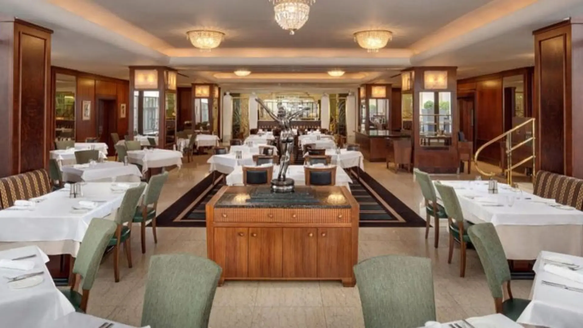 Art Deco restaurant with chandeliers, white tables, and a bronze statue.