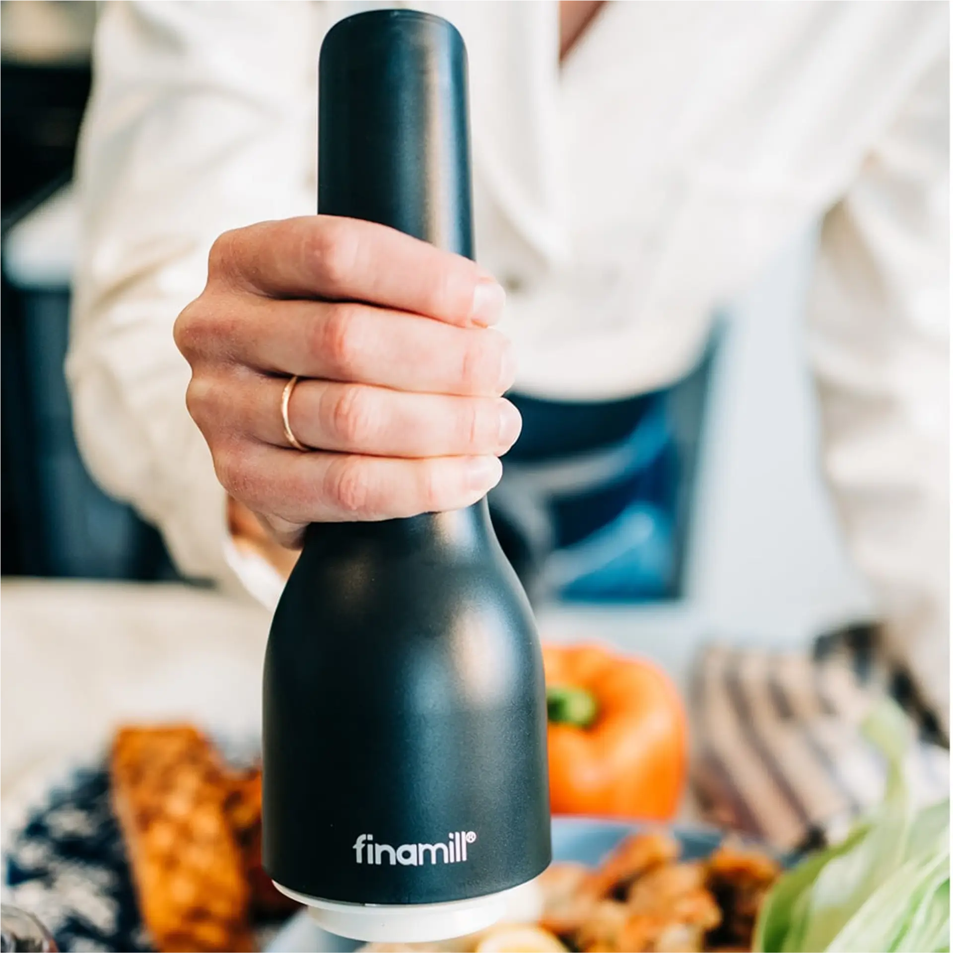 Hand holding black FinaMill grinder over a plate of food.