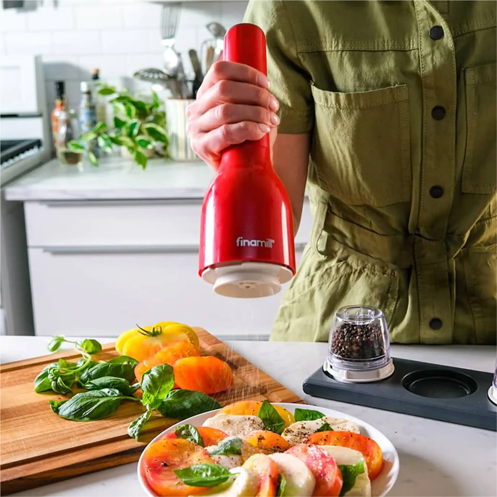 Hand holding red FinaMill grinder over a caprese salad.