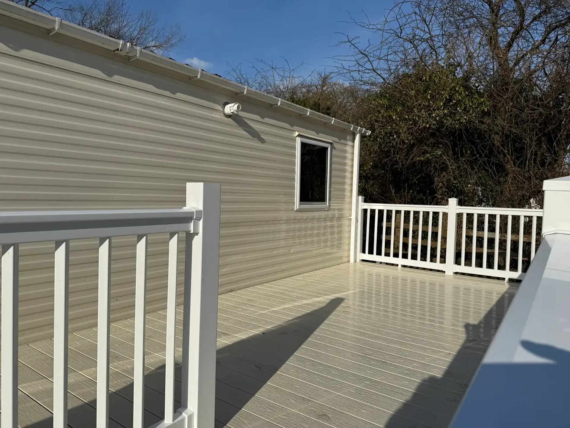 Empty decking area beside the holiday home, trees in the background.