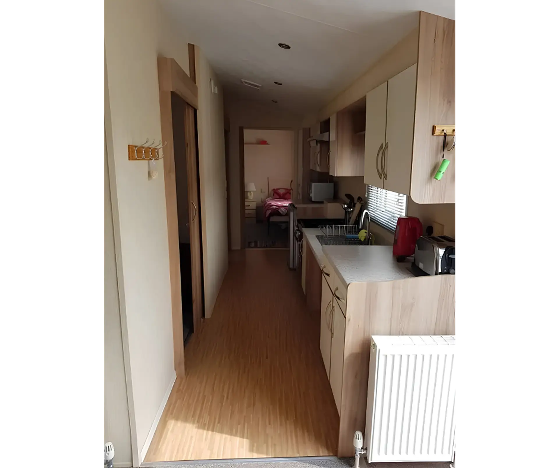 Hallway leading past kitchen units toward a bedroom, viewed from the entrance.