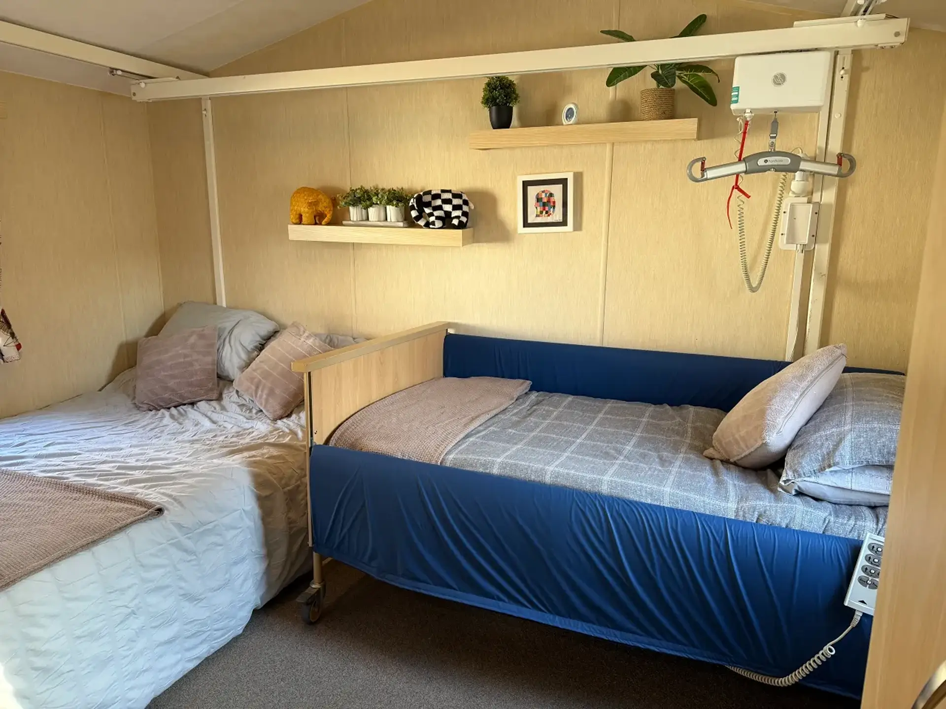 Bedroom with an adjustable hospital-style bed beside a double bed, ceiling hoist track above.