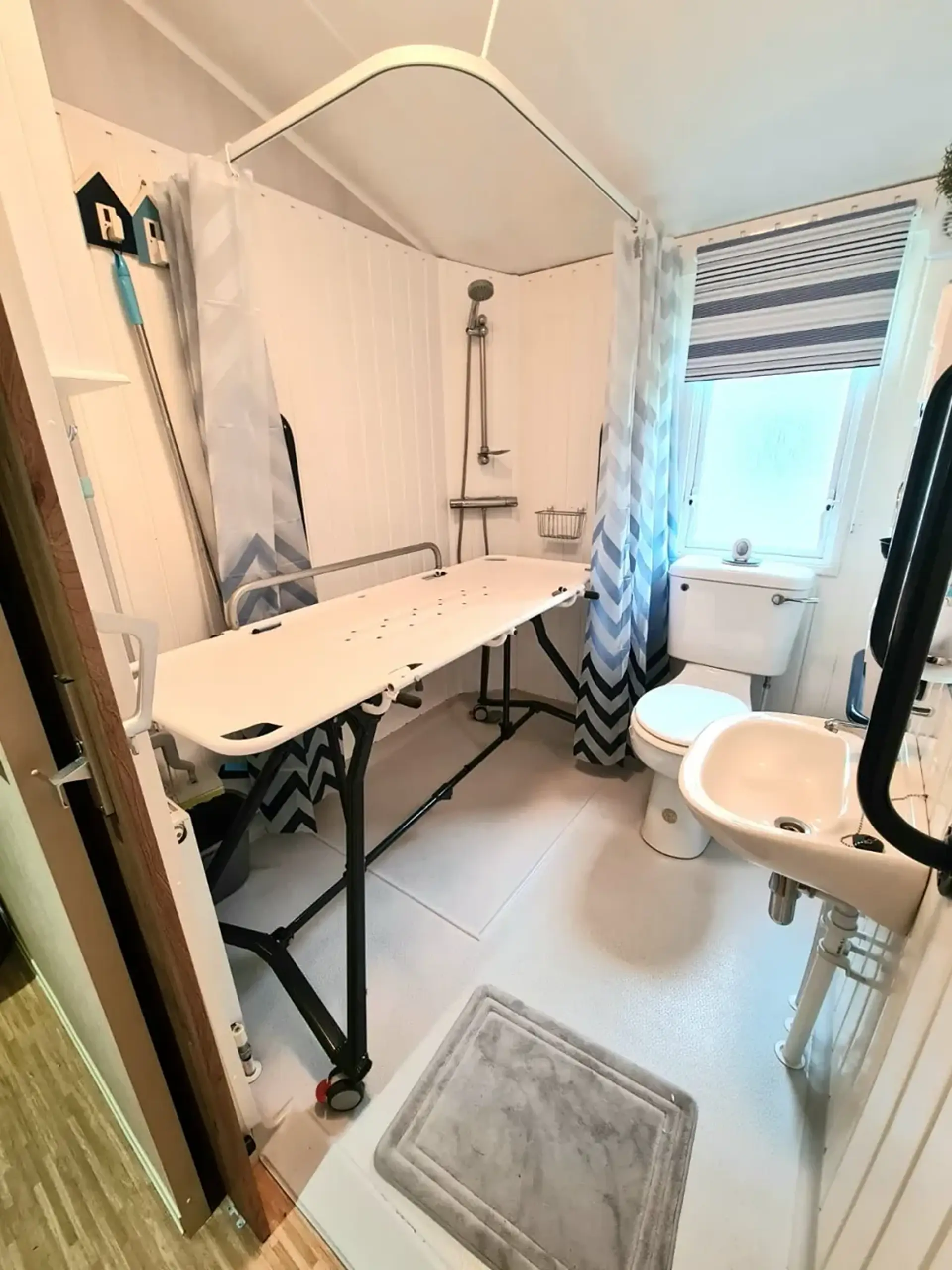 Wet room with a height-adjustable shower changing table, toilet and sink.