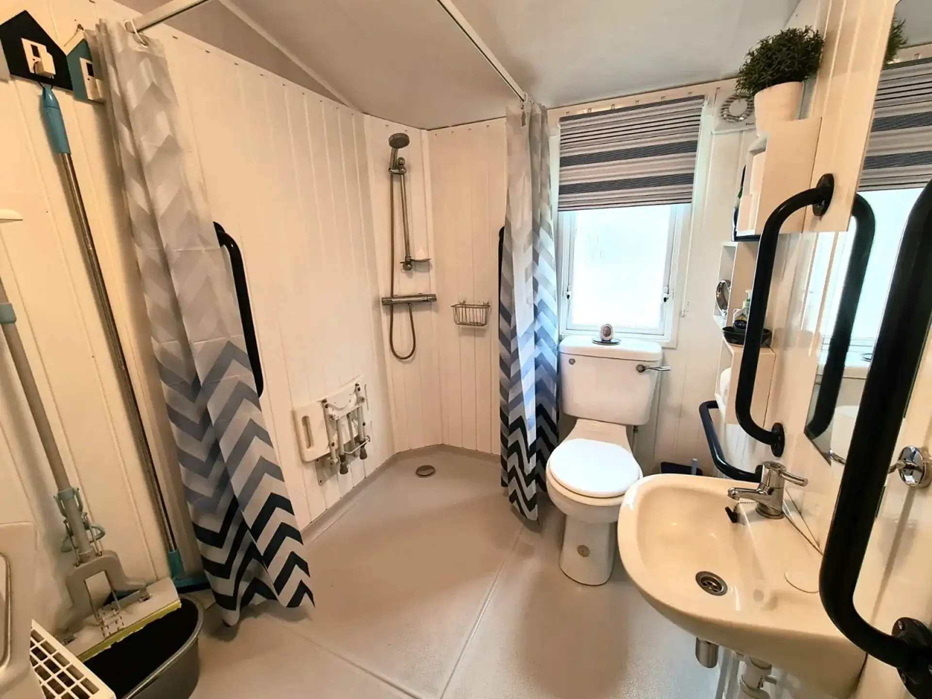 Wet room with fold-down shower seat, toilet and sink, striped blind at the window.
