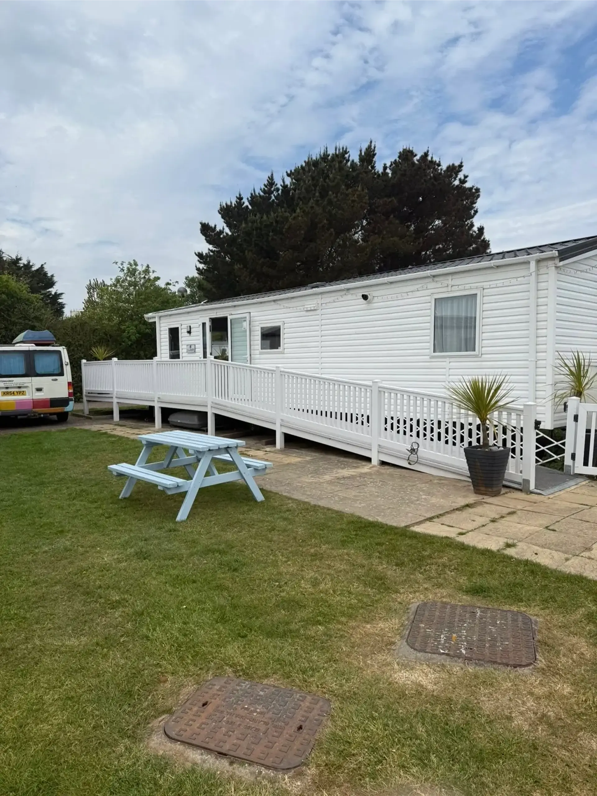 White holiday home with a long access ramp, picnic bench on the lawn.