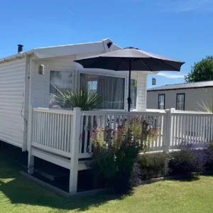 White holiday home with a covered veranda, black umbrella and flowering plants.