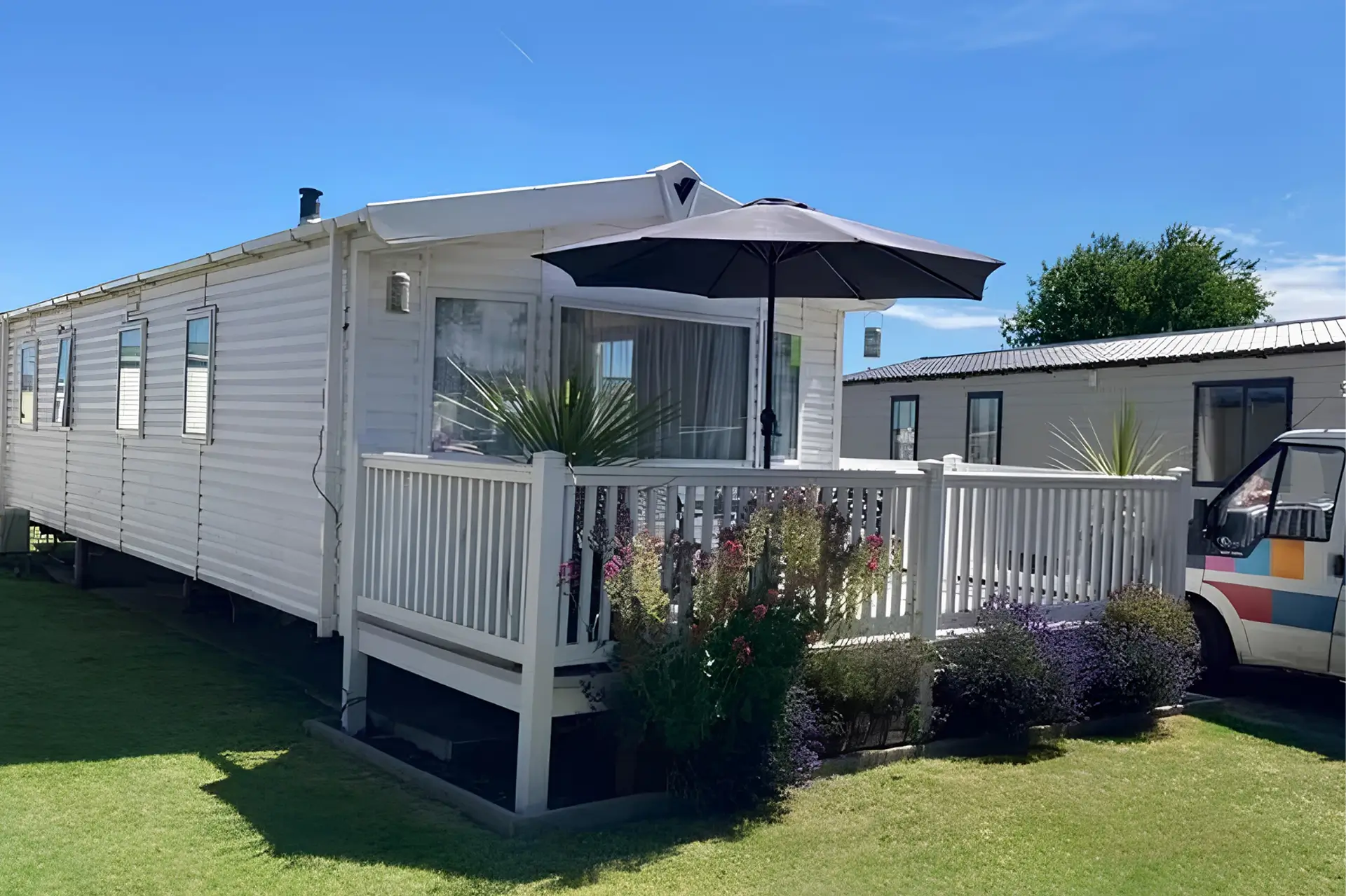 White holiday home with a covered veranda, black umbrella and flowering plants.