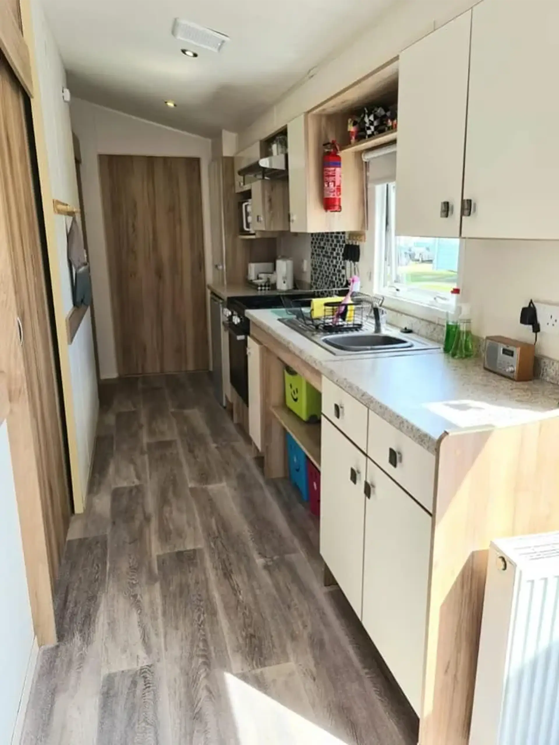 Kitchen with sink, cooker and cupboards, hallway leading to a wooden door.