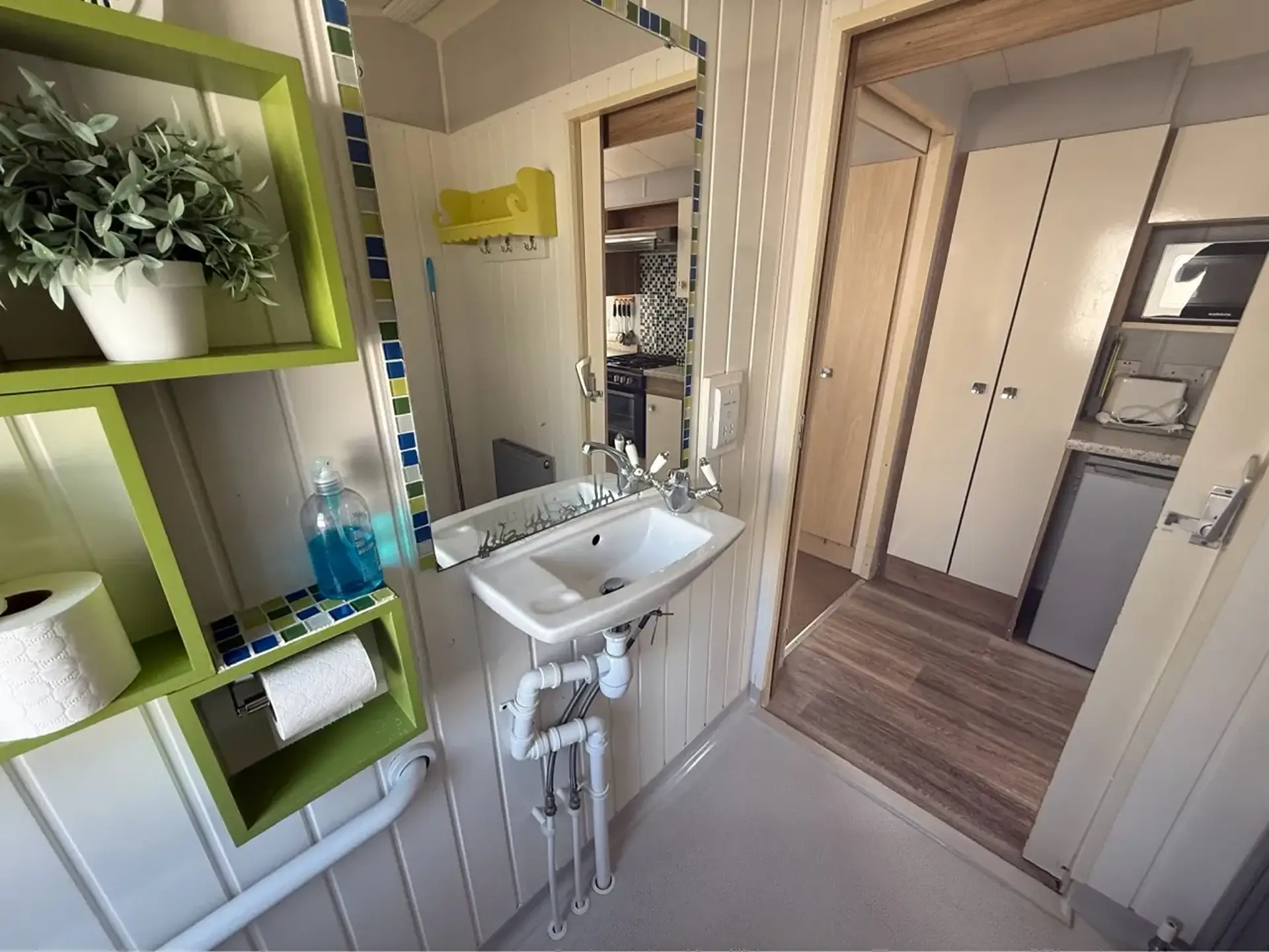 Hallway with sink, mirror and shelving leading to the kitchen and bedrooms.
