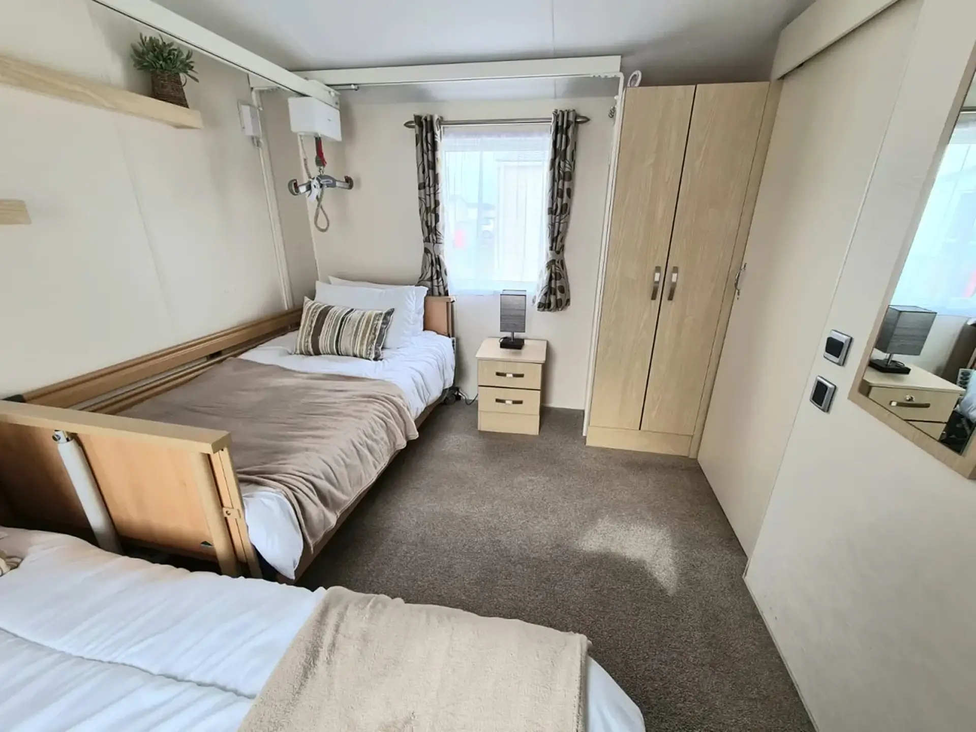 Bedroom with an adjustable hospital-style bed beside a standard bed, ceiling hoist above.
