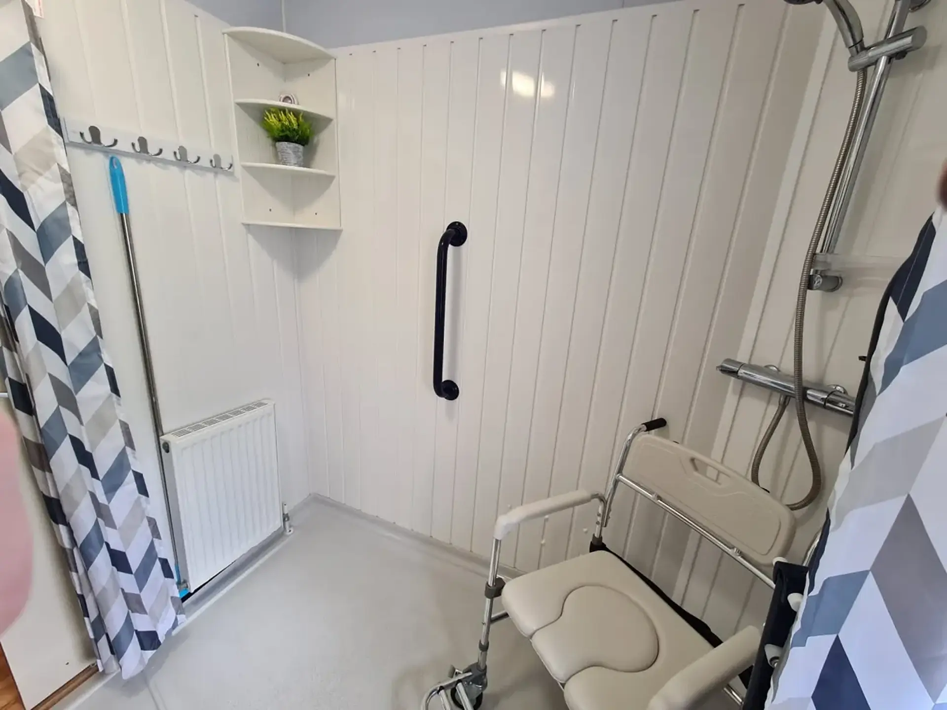 Wet room with a mobile shower/commode chair, grab rail and shower fittings.