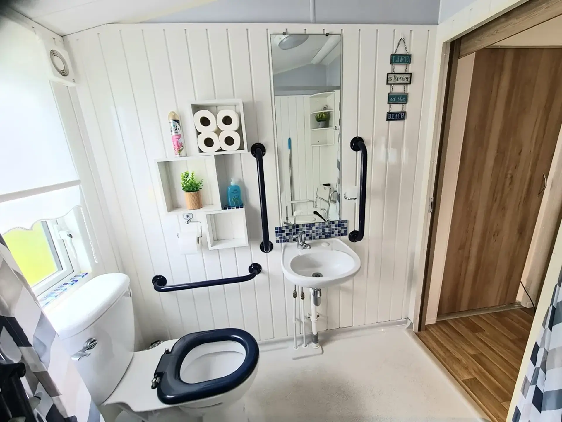 Wet room with toilet, sink and black grab rails, mirror on the wall.