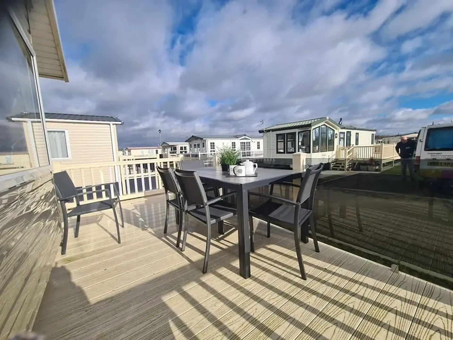 Decking area with a dining table and chairs, other holiday homes visible beyond.
