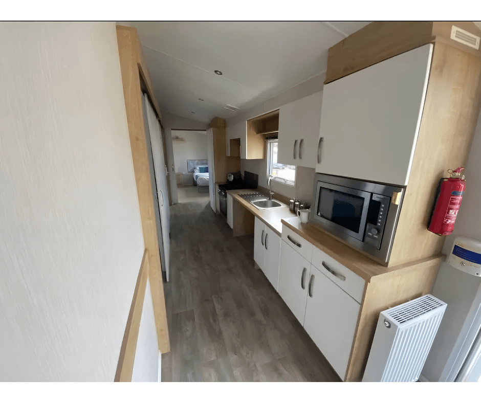 Galley kitchen with sink, hob, microwave, and bedroom beyond.