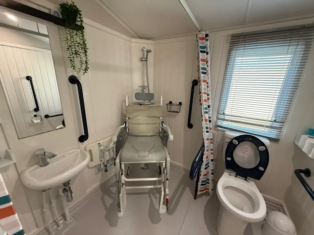 Bathroom with wheeled shower/commode chair, sink, and toilet.
