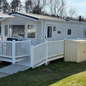 Beige static holiday home with wraparound ramp, decking, and storage shed.