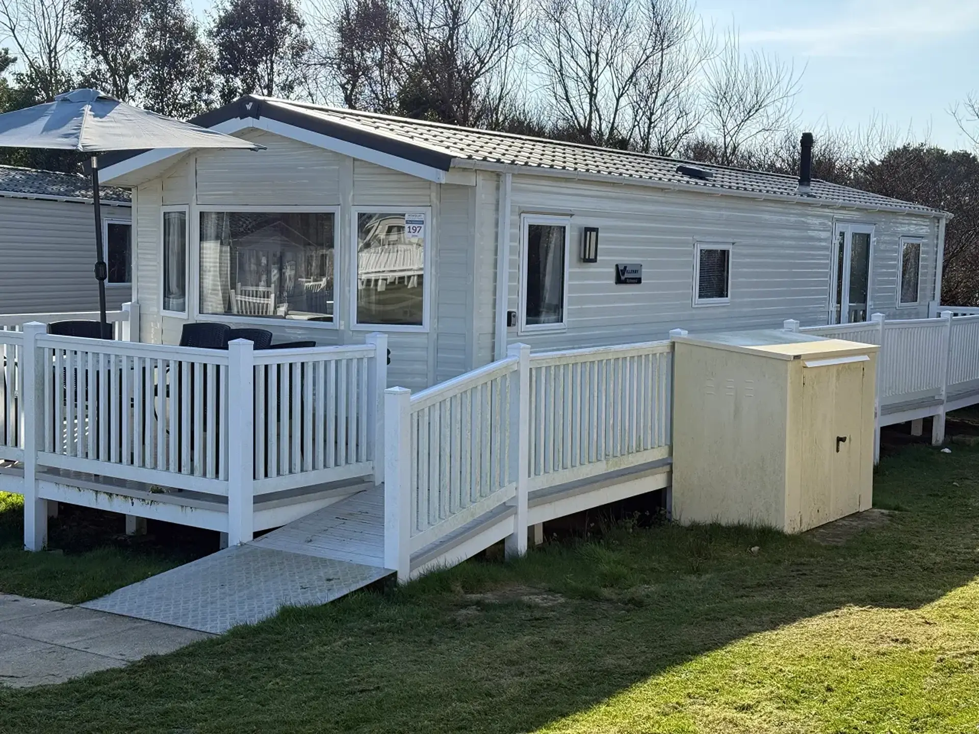 Beige static holiday home with wraparound ramp, decking, and storage shed.