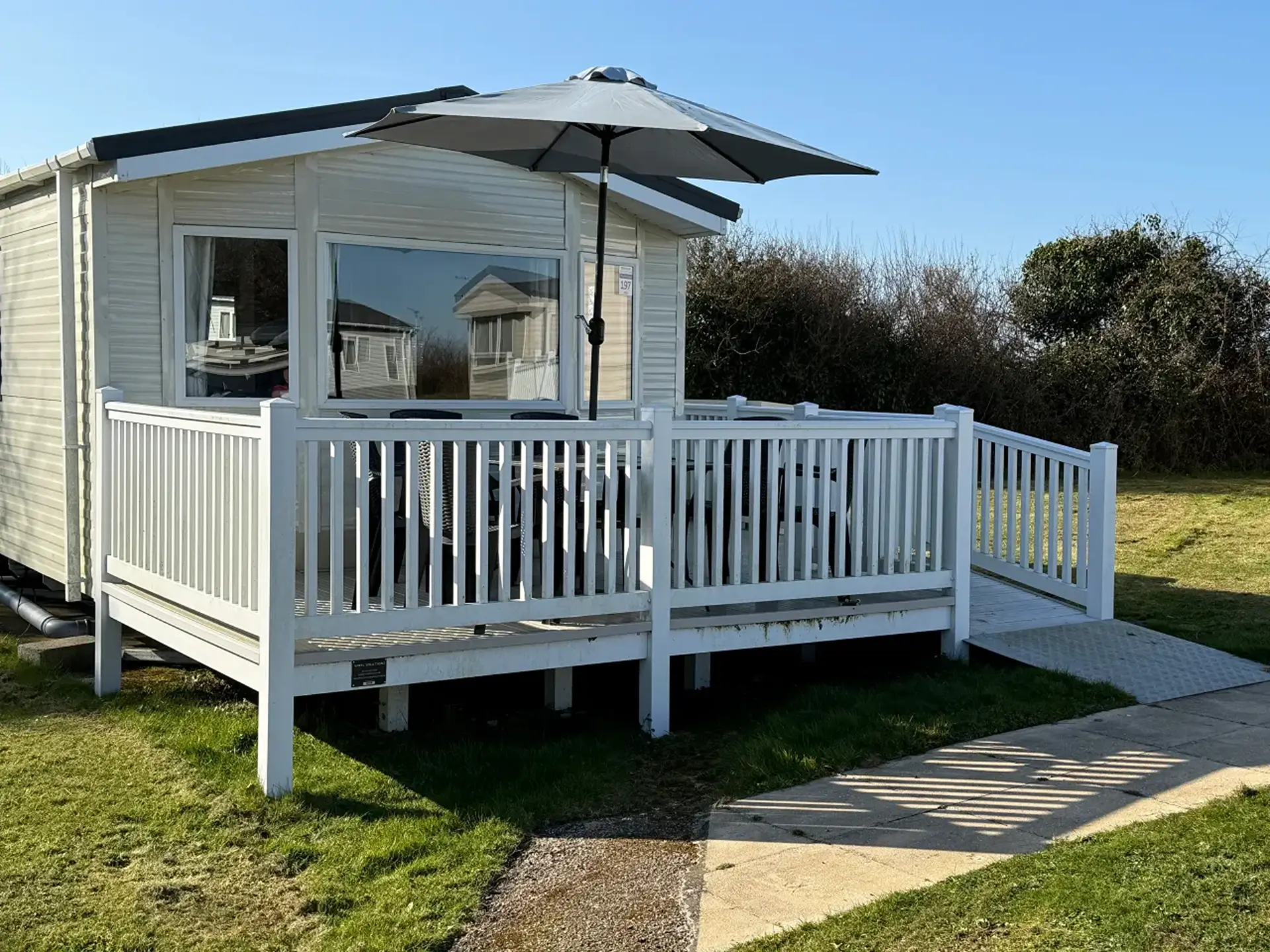 Static holiday home decking with dining set, parasol, and access ramp.