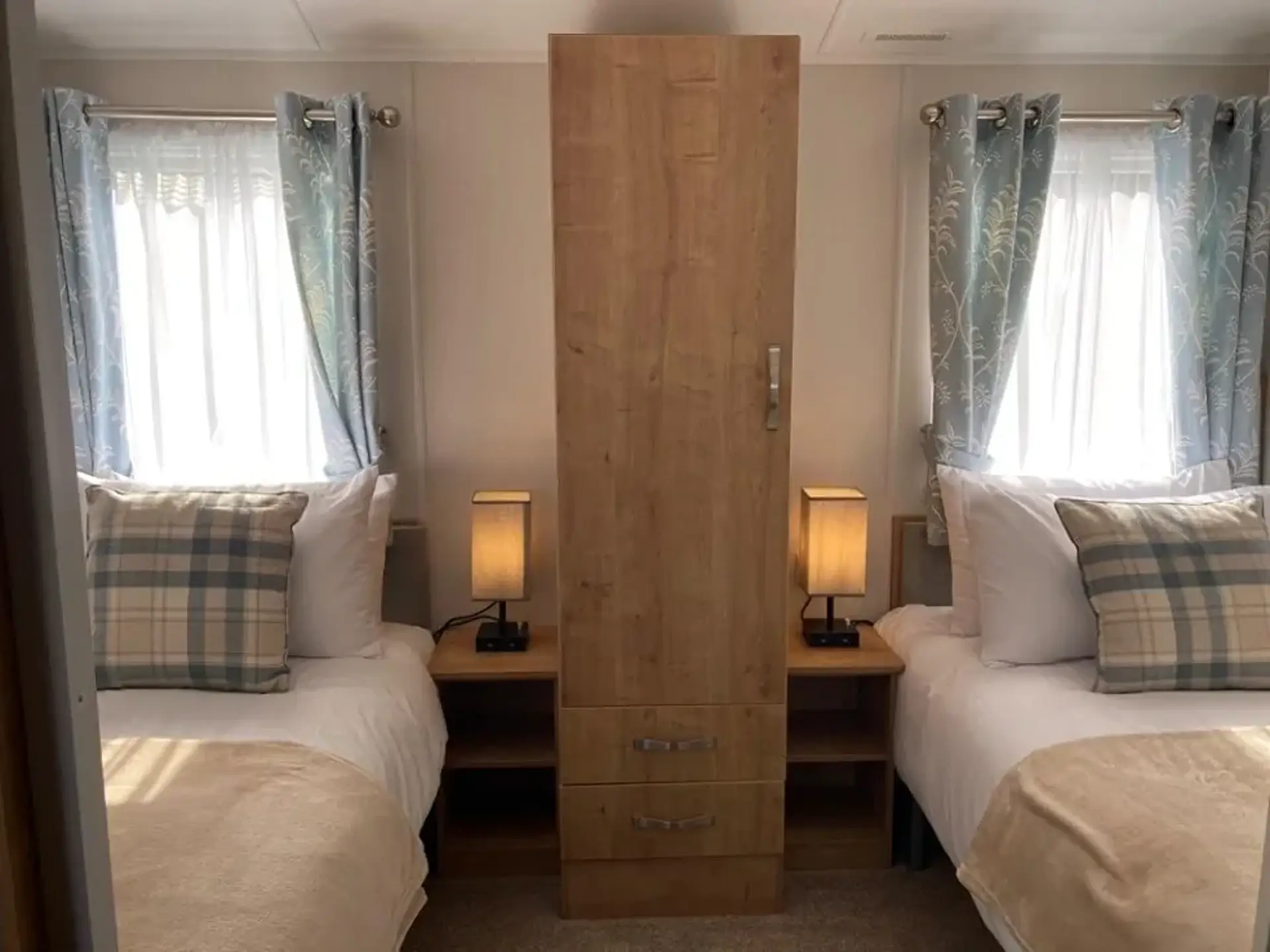 Twin beds either side of a tall wardrobe with bedside lamps.