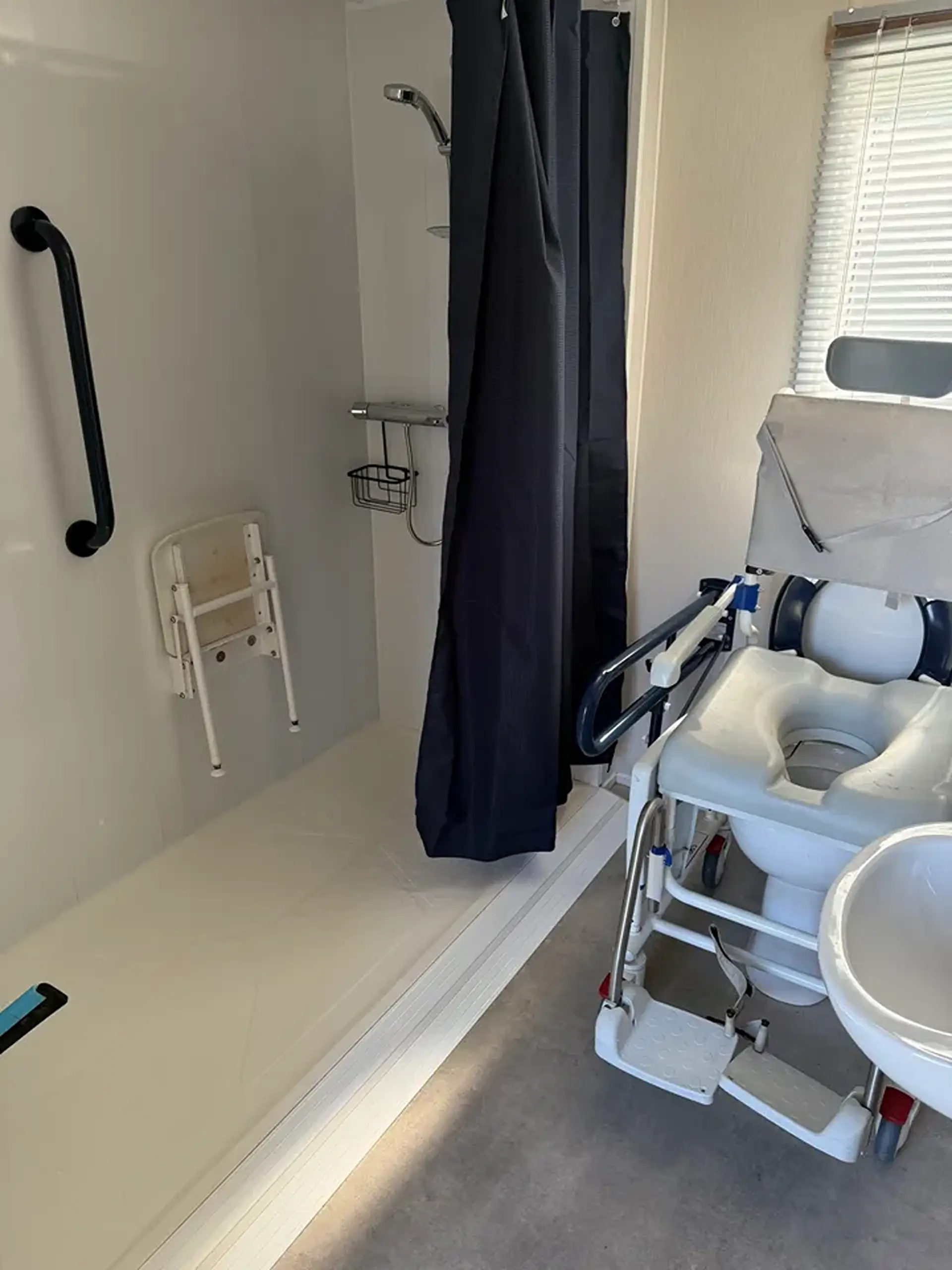 Wet room shower area with fold-down seat next to a shower/commode chair.