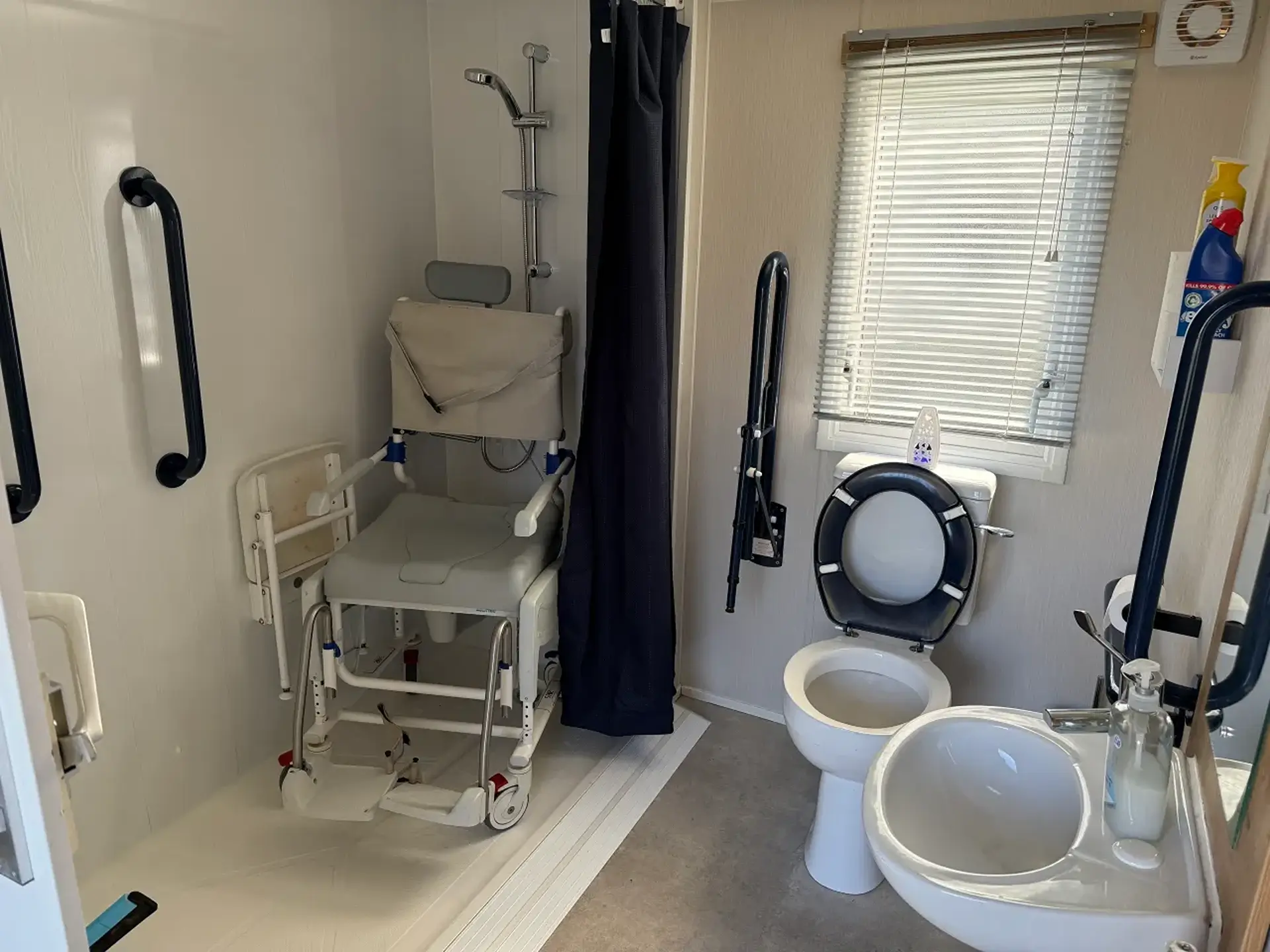 Wet room with shower chair, toilet, and grab rails.