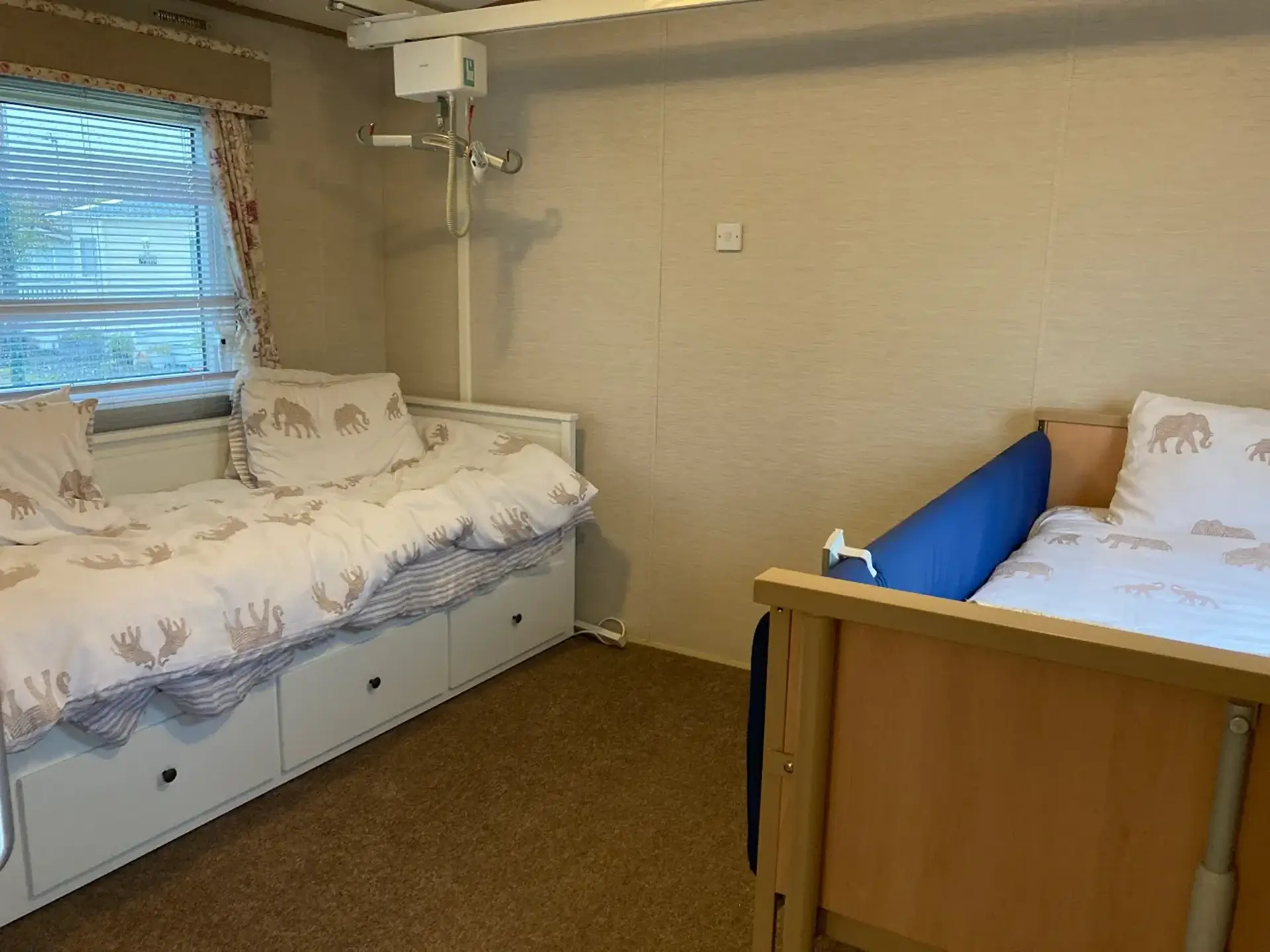 Bedroom with standard bed, ceiling hoist, and adjustable bed alongside.