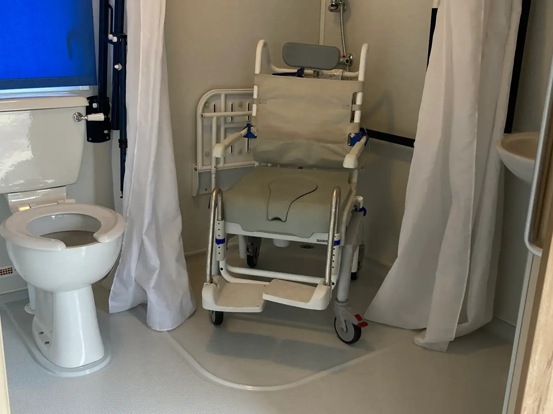 Bathroom with toilet and wheeled shower/commode chair.