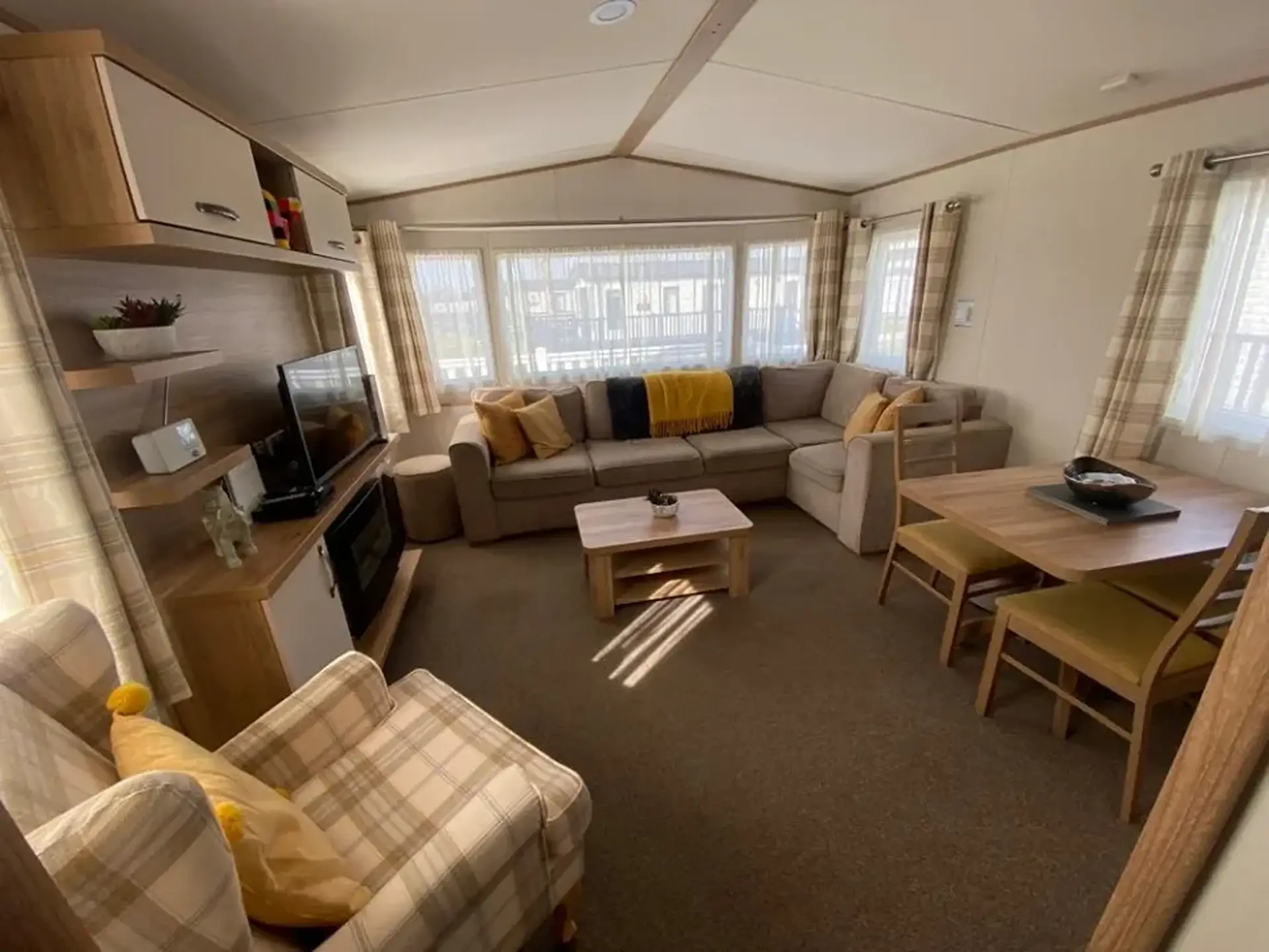 Open-plan lounge with beige corner sofa, armchair, dining table, and TV unit.