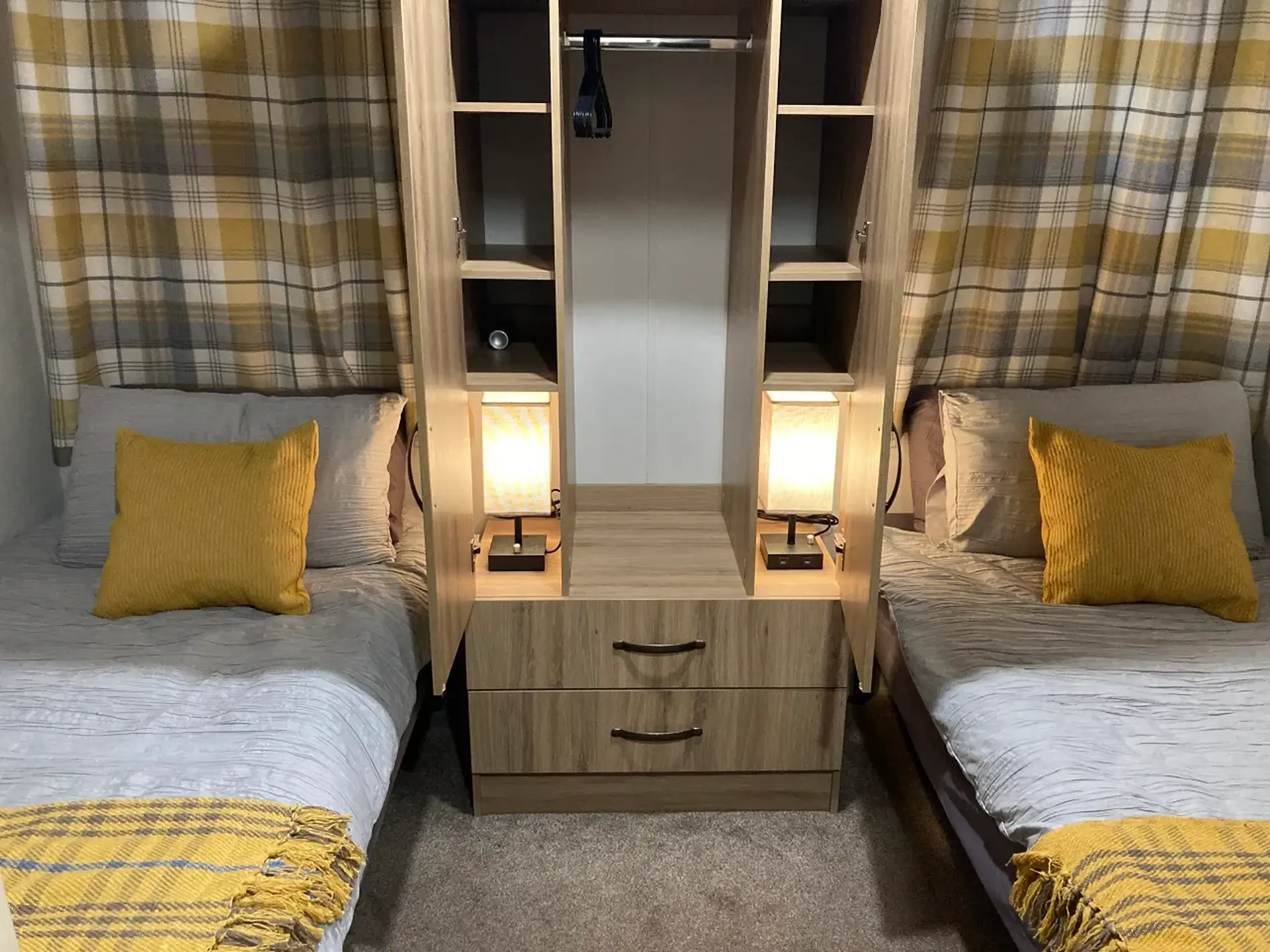 Twin beds either side of an open wardrobe with built-in lamps and drawers.