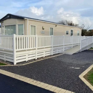 Beige static holiday home with wraparound decking, ramp, and railings.