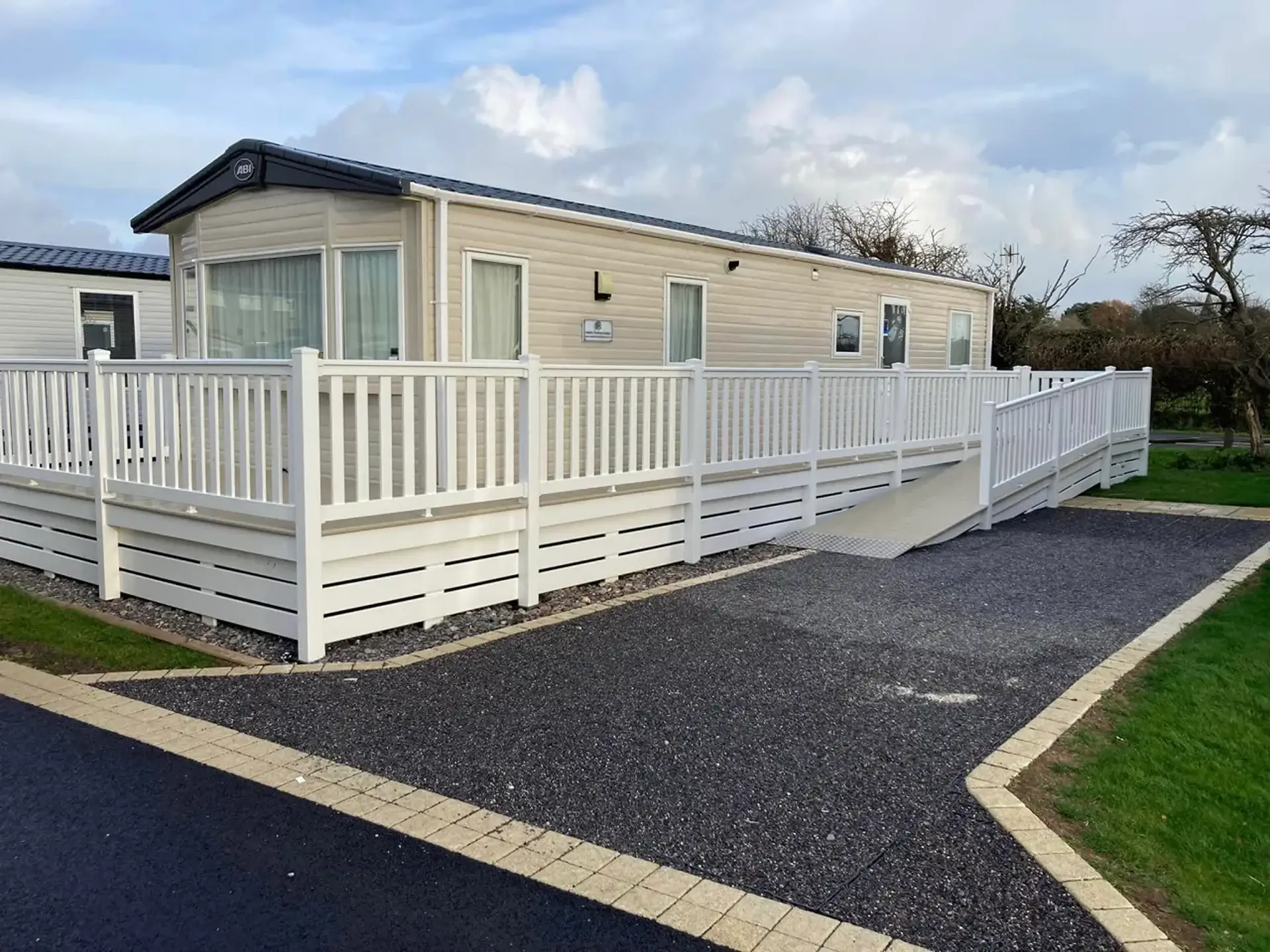 Beige static holiday home with wraparound decking, ramp, and railings.