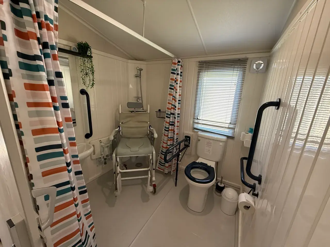 Wet room with shower/commode chair, toilet, and grab rails.