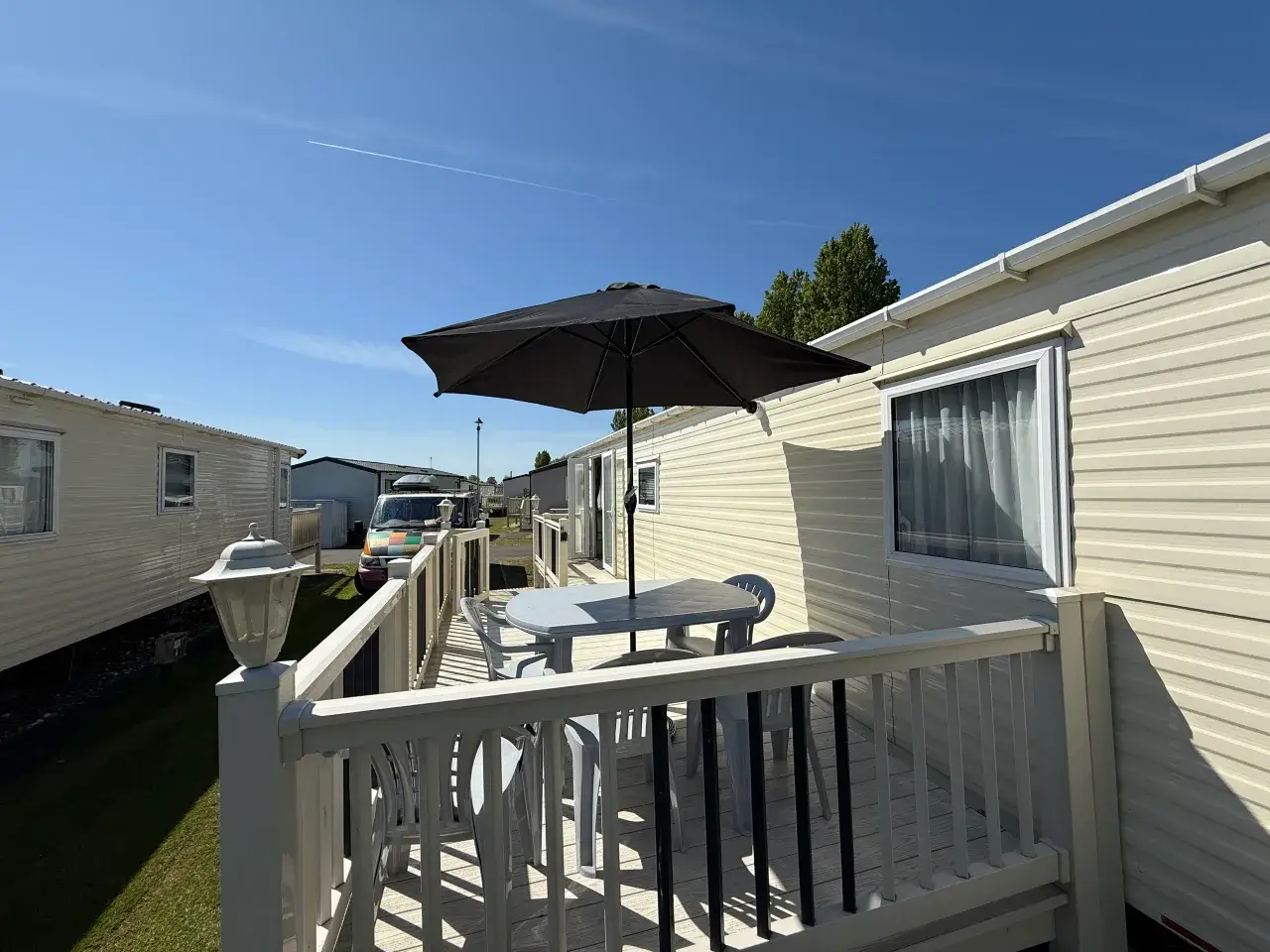 Caravan decking with table, chairs, and parasol between units.