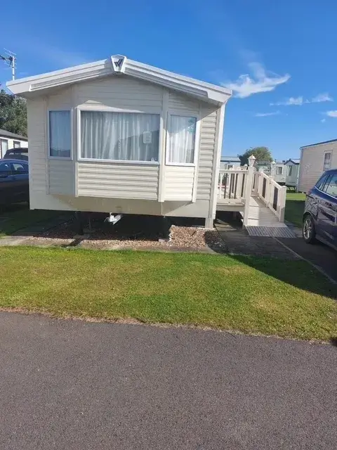 Beige static caravan with ramp and small decking area.
