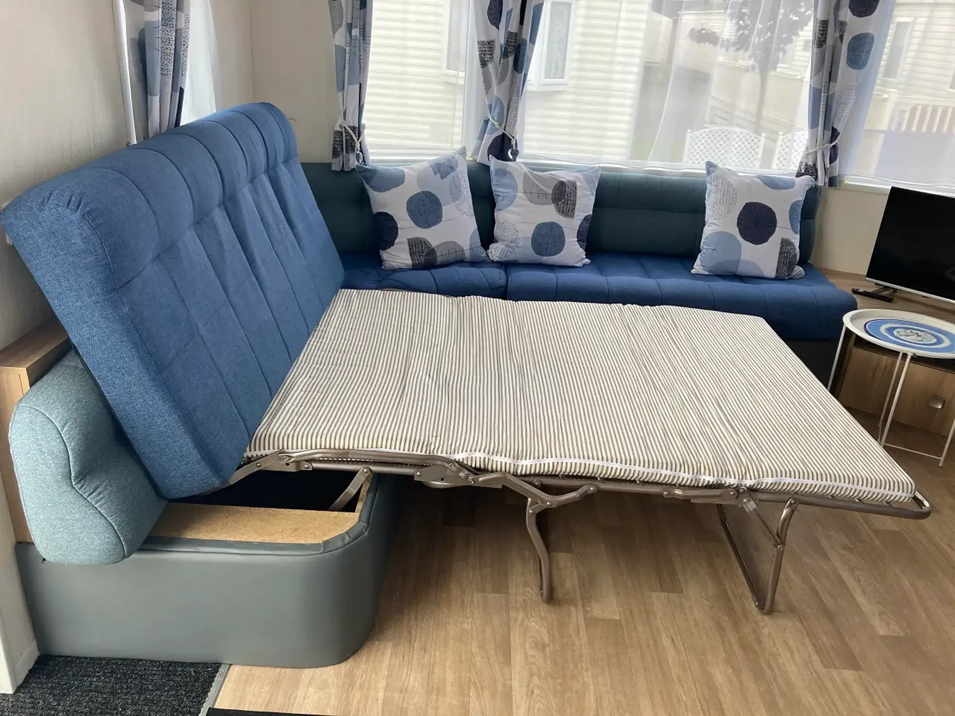 Corner sofa with fold-out bed extended, striped mattress, blue upholstery.