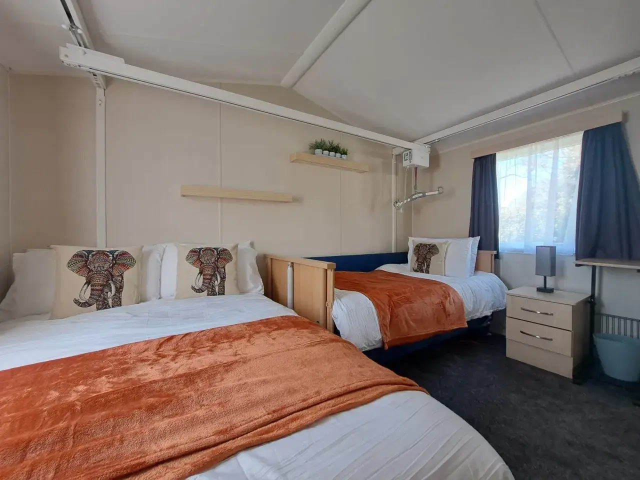 Twin room with adjustable bed, ceiling hoist, and bedside cabinet.