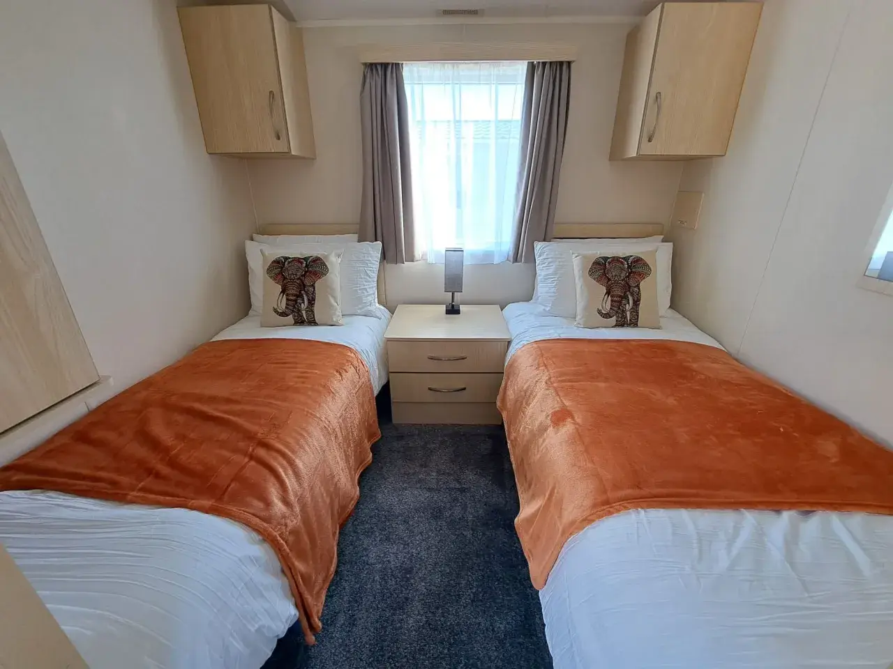 Twin beds with orange throws either side of a bedside cabinet.