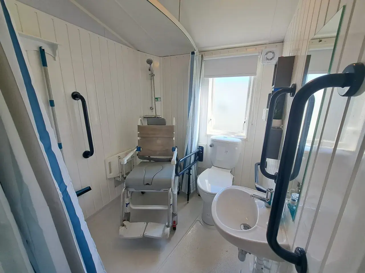 Bathroom with wheeled shower/commode chair, toilet, and sink.