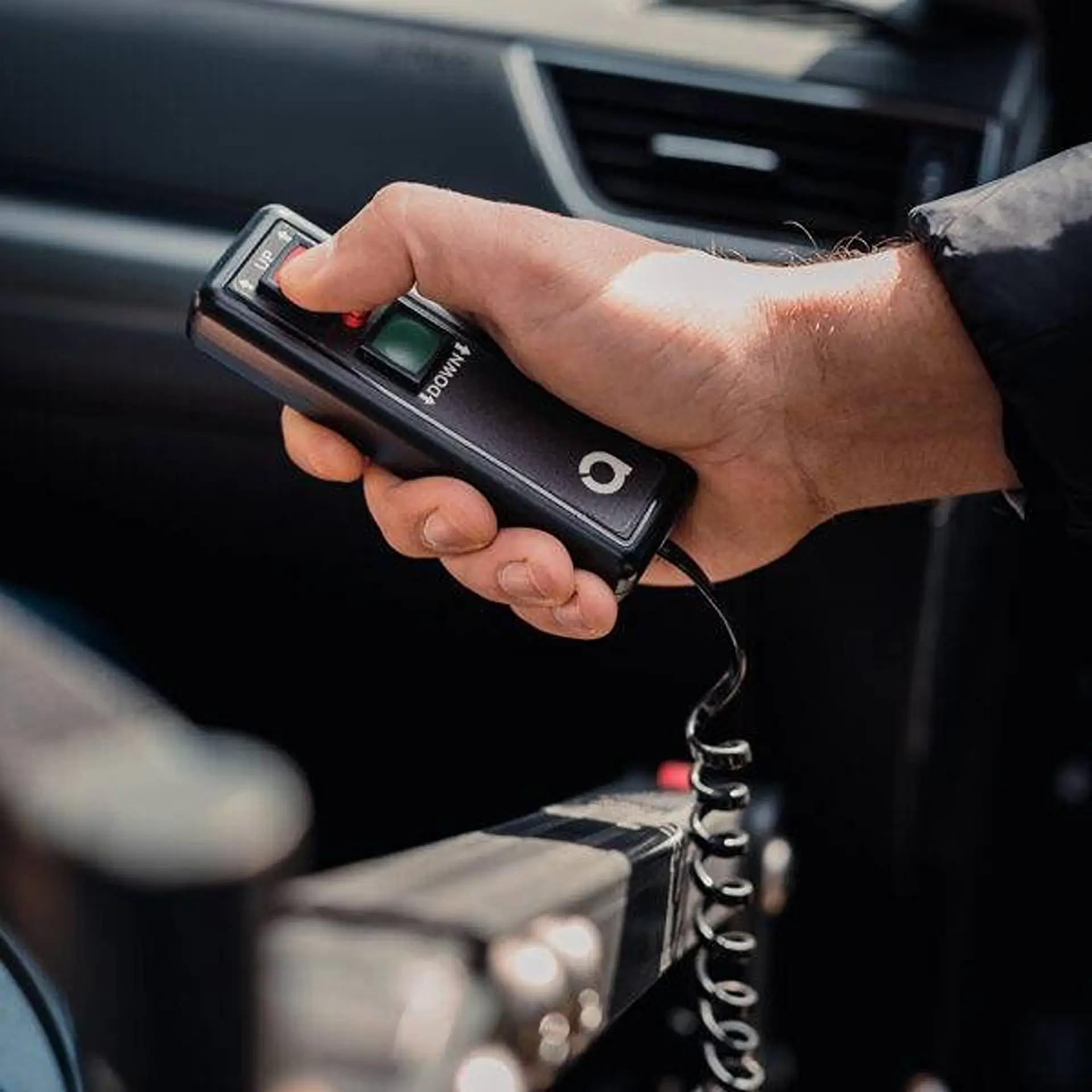 Close-up of a hand holding the up/down hoist remote control inside a car.