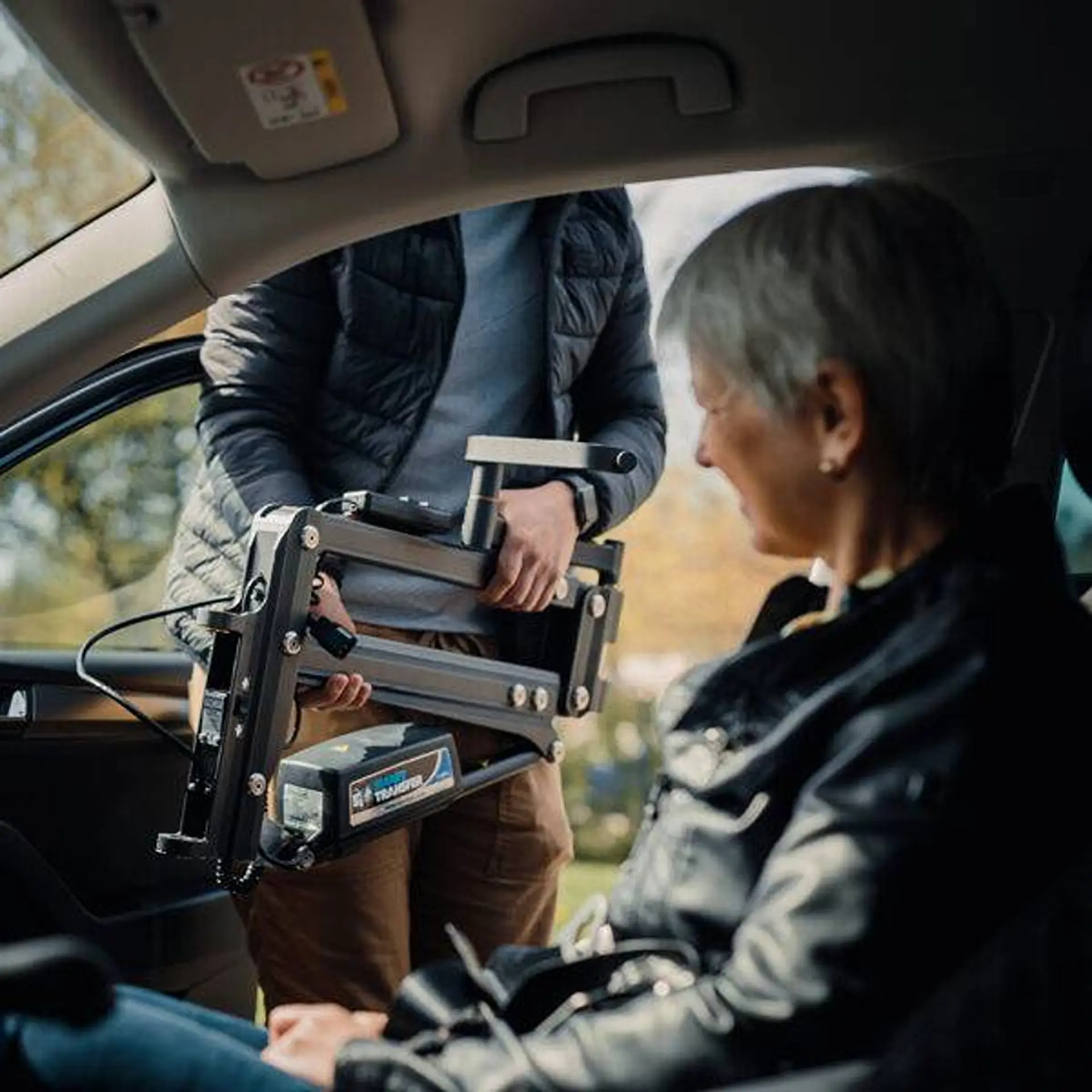 Man holding the folded hoist arm and sling beside a woman seated in the car.