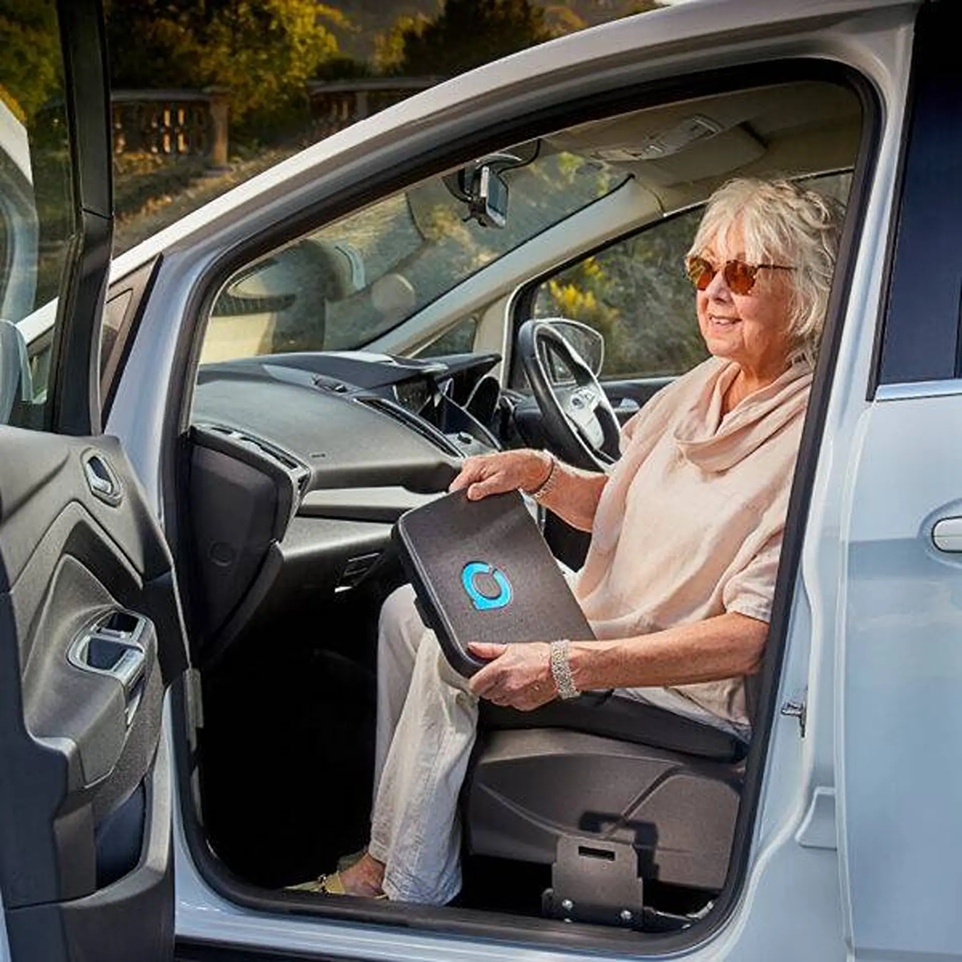 Older woman seated in her car with feet on the transfer plate, smiling toward camera.