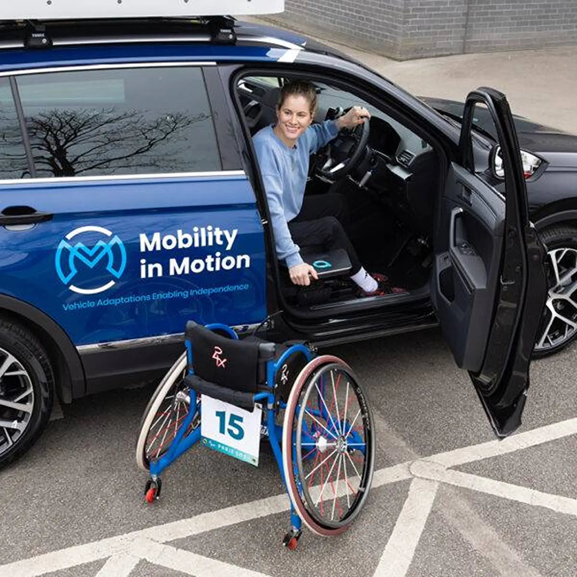 Woman in wheelchair-accessible parking bay transferring from her wheelchair into the driver's seat via the transfer plate.