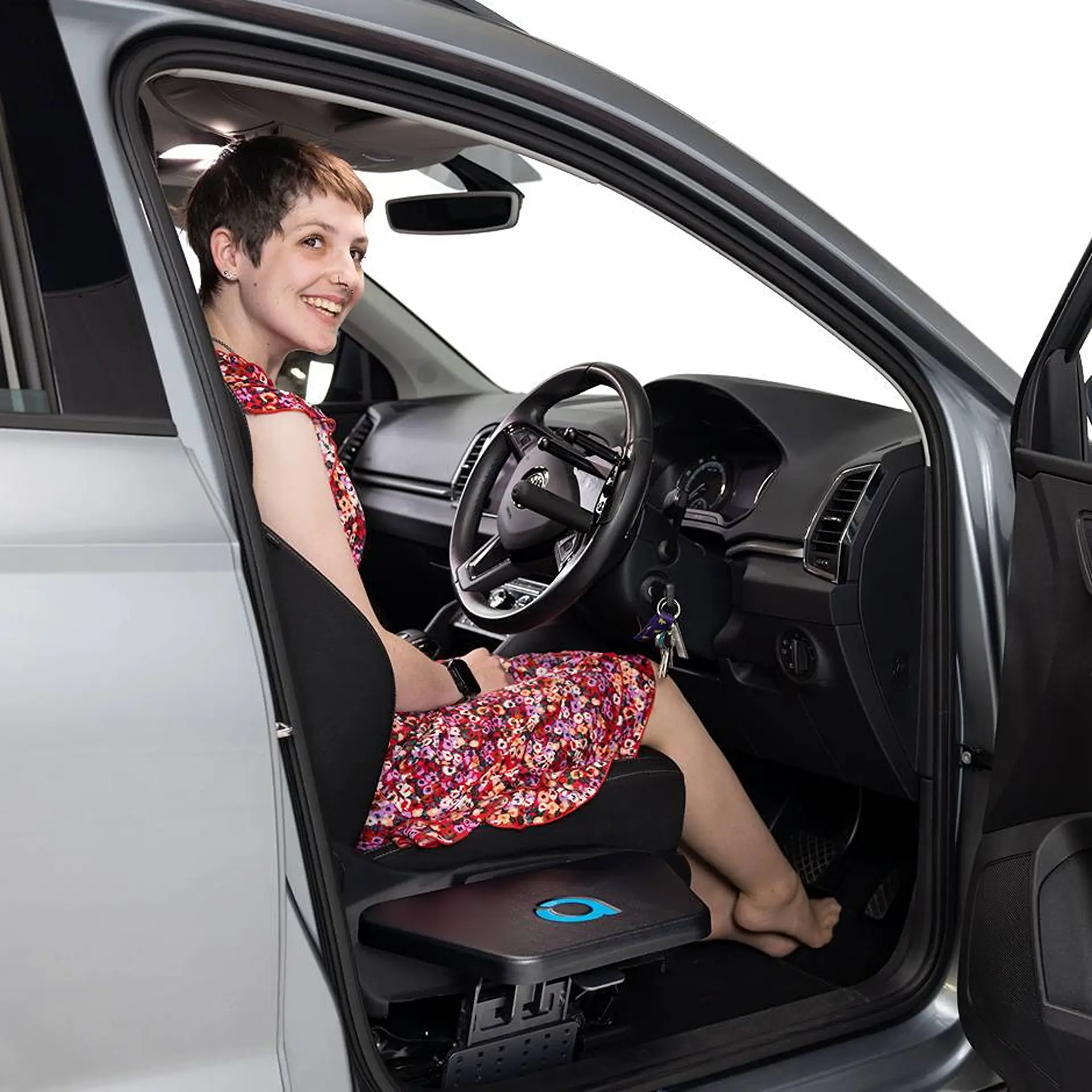 Woman smiling in driver's seat with feet on the transfer plate, studio white background.
