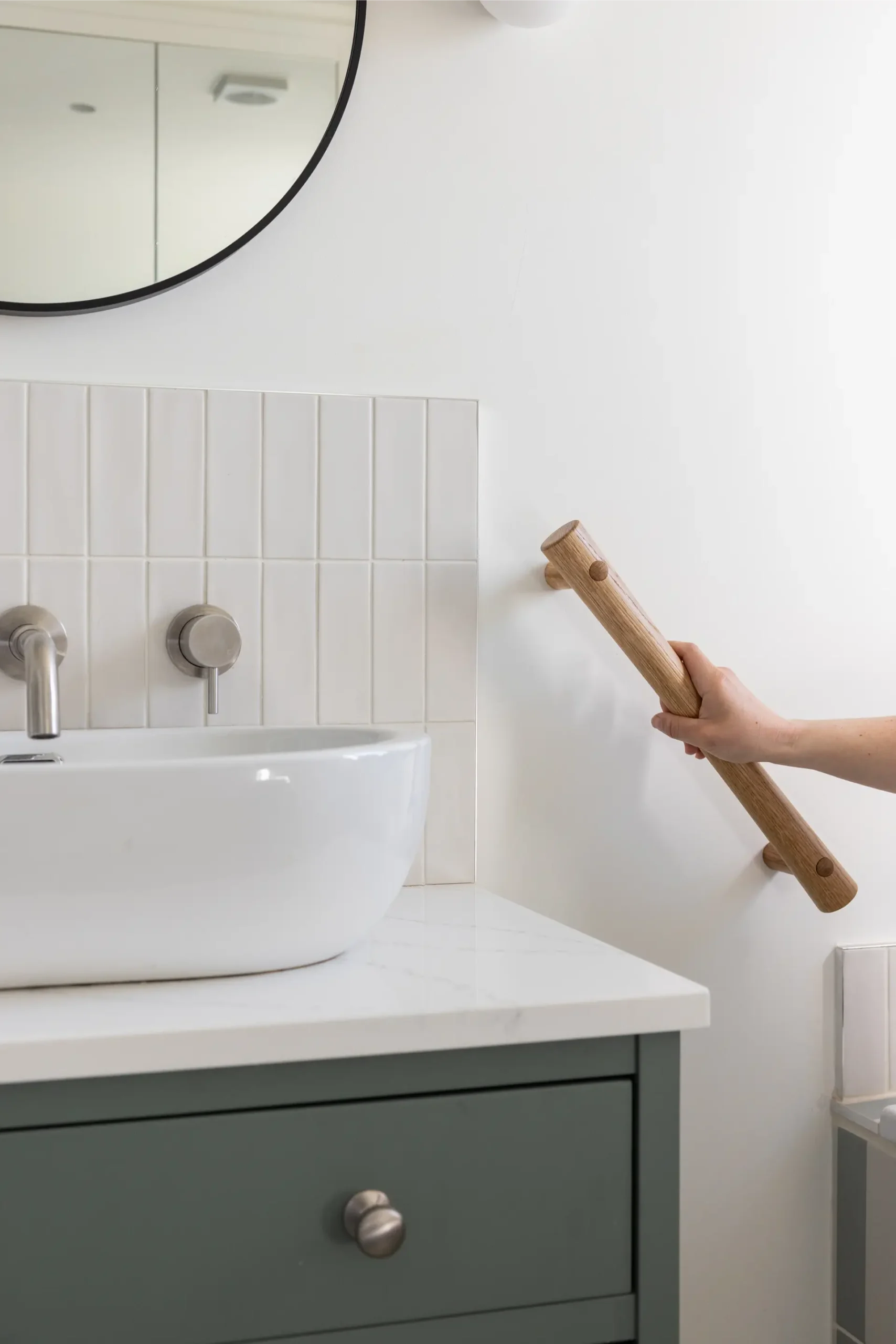 Hand gripping an oak grab rail beside a bathroom vanity sink and mirror.